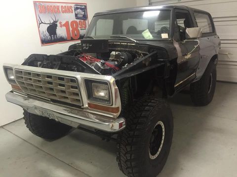 1979 Ford Bronco - Black square-body Ford Bronco mid-build in a garage, hood removed exposing engine, chrome grille, K&N air filter, beer promo sign on wall.