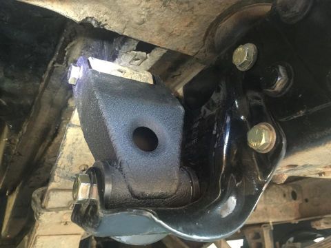 1979 Ford Bronco - A close-up, low-angle shot shows a black aftermarket suspension component bolted to the underside of a vehicle frame. The part features a b…