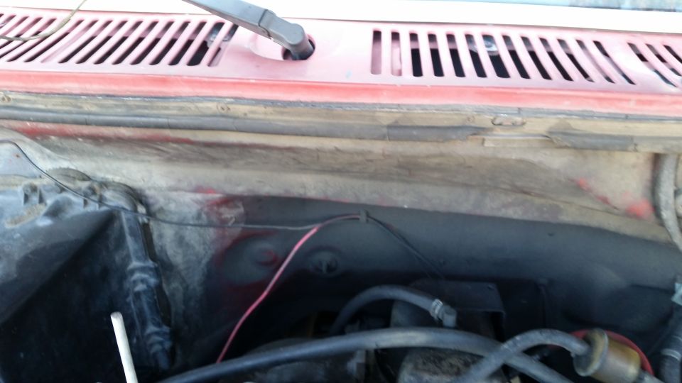 Red vehicle engine bay with hoses, wires, and windshield wiper assembly.