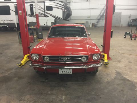 1965 Ford Mustang - A red 1965 Ford Mustang is parked in a garage, positioned on a car lift. The front of the classic car is facing the camera, with its headli…