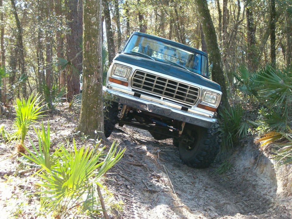 Dark blue 1978 Ford Bronco off-roading on a dirt path, front 3/4 view