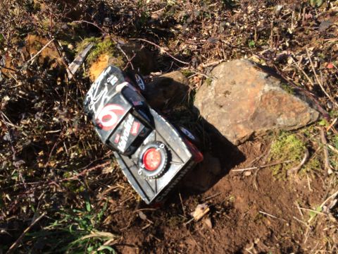 1989 Ford Bronco - black-and-red number 6 die-cast or RC car resting in dirt beside a rock in outdoor brush.