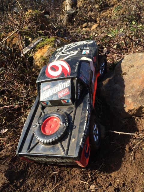 1989 Ford Bronco - A black remote-controlled off-road truck with red and white decals is positioned on a dirt and rocky terrain.