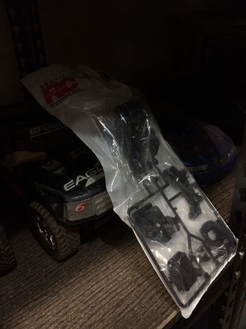1989 Ford Bronco - A black RC car with "BFGoodrich" and "EAGLE" text on the side is partially covered by a plastic bag of unassembled parts. Another blue RC c…