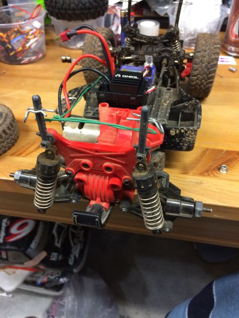 1989 Ford Bronco - A close-up, overhead view of the chassis and suspension of an RC car, showing a red plastic component, a black electronic speed controller,…