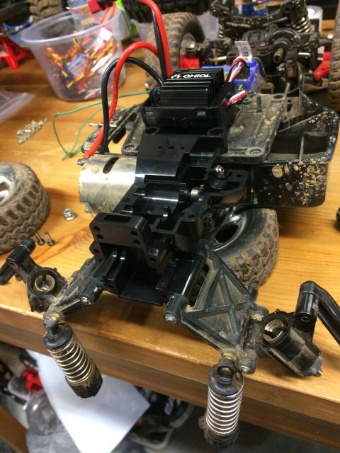 1989 Ford Bronco - A partially disassembled RC car chassis is shown on a wooden surface. The chassis features a black electronic speed controller with red and…