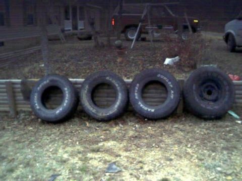 1986 Ford Bronco - Four tires are lined up on the ground, three with visible tire branding.