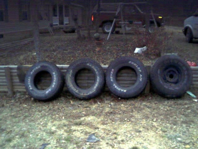 Four tires lined up on the ground. Three have text: RADIAL ROVER and DUNLOP A/T