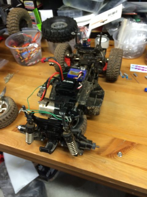 1989 Ford Bronco - A disassembled remote-controlled car chassis with its wheels, shocks, and electronic components visible on a wooden surface. Various parts…