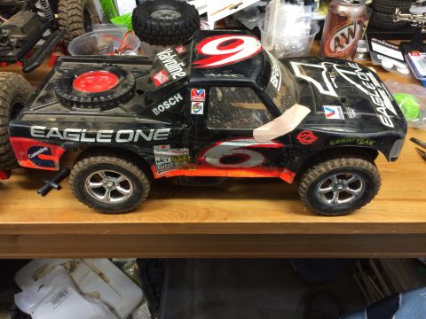 1989 Ford Bronco - A black remote-controlled truck with red and orange graphics is shown on a wooden surface, possibly a workbench. The truck has "EAGLE ONE"…