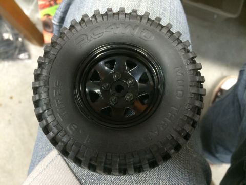 1989 Ford Bronco - A close-up overhead view of a black RC4WD Mud Thrasher tire with a black rim, mounted on a person's leg wearing blue jeans.