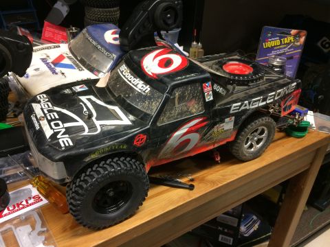 1989 Ford Bronco - A black remote-controlled monster truck with "EAGLE ONE" and "Cummins" decals sits on a wooden table. Other RC car parts and accessories ar…