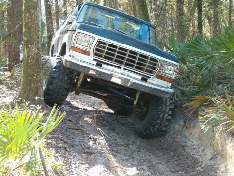 1991 Ford Bronco - This lifted Ford Bronco navigates a challenging off-road path through a wooded area.
