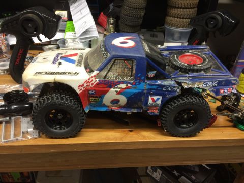 1989 Ford Bronco - A modified remote-controlled off-road truck with a blue and white body, featuring "BFGoodrich" and "Valvoline" decals, sits on a wooden wor…