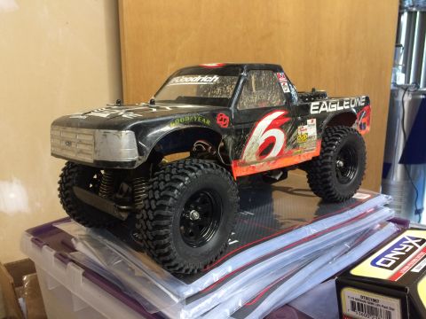 1989 Ford Bronco - A black remote-controlled pickup truck with large off-road tires sits on top of a stack of plastic packaging. The truck has red and white r…