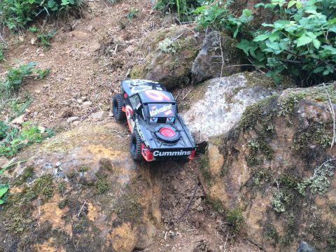 1989 Ford Bronco - A remote-controlled rock crawler truck with "Valvoline" and "Cummins" decals is navigating a rocky, wooded trail.