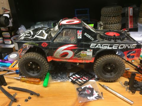 1989 Ford Bronco - A black remote-controlled off-road truck with red and white decals sits on a wooden workbench surrounded by tools and spare parts. The truc…