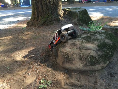 1989 Ford Bronco - A remote-controlled rock crawler vehicle with orange and black accents is positioned on a large moss-covered rock. The vehicle is angled to…