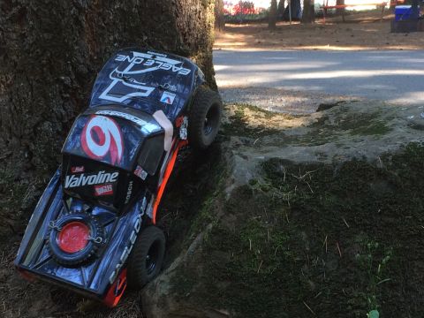 1989 Ford Bronco - A remote-controlled toy truck with a black body and orange accents is positioned on a mossy rock next to a tree. The truck features racing…