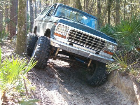 1991 Ford Bronco - This modified Ford Bronco is navigating a challenging off-road trail with steep inclines and loose dirt.