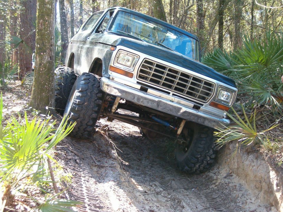 Ford Bronco with large tires climbing a dirt hill in a wooded area