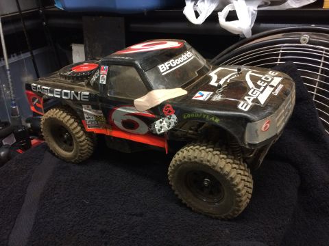 1989 Ford Bronco - A black remote-controlled monster truck with "EAGLE ONE" decals is shown from a 3/4 front angle, resting on a dark fabric surface.