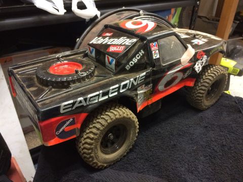 1989 Ford Bronco - A dusty, black remote-controlled "Street Truck" replica with red and orange racing decals sits on a dark blue towel. The truck has a spare…