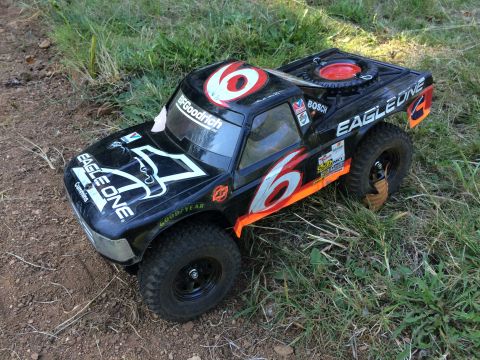 1989 Ford Bronco - A black remote-controlled monster truck with "EAGLE ONE" and "6" graphics is parked on dirt and grass. The truck has large off-road tires a…