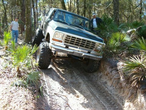 1991 Ford Bronco - A modified Ford Bronco navigates a steep, sandy incline in a wooded area.