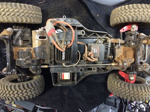 1989 Ford Bronco - A top-down view of the chassis and drivetrain of a remote-controlled off-road vehicle, heavily covered in dirt and dust. Visible components…