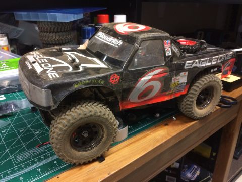 1989 Ford Bronco - A black remote-controlled monster truck with "Eagle One" and "BFGoodrich" decals sits on a wooden shelf next to a green cutting mat. The tr…