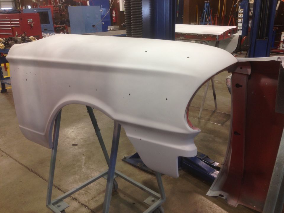 Primed white car fender on a stand in a workshop.