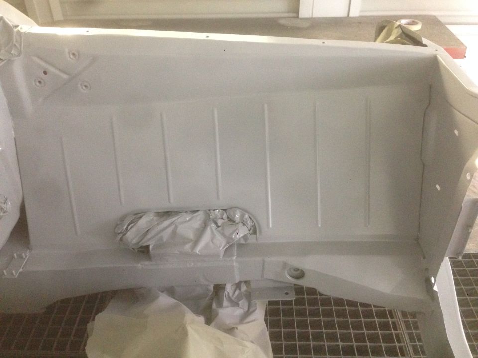 Underside of a vehicle coated in gray primer, with protective coverings.