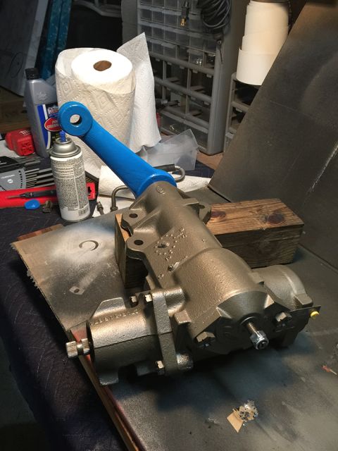 1978 Ford Bronco - A rebuilt power steering gearbox, painted metallic gray, is shown with a bright blue painted pitman arm. The part is resting on a workbench…