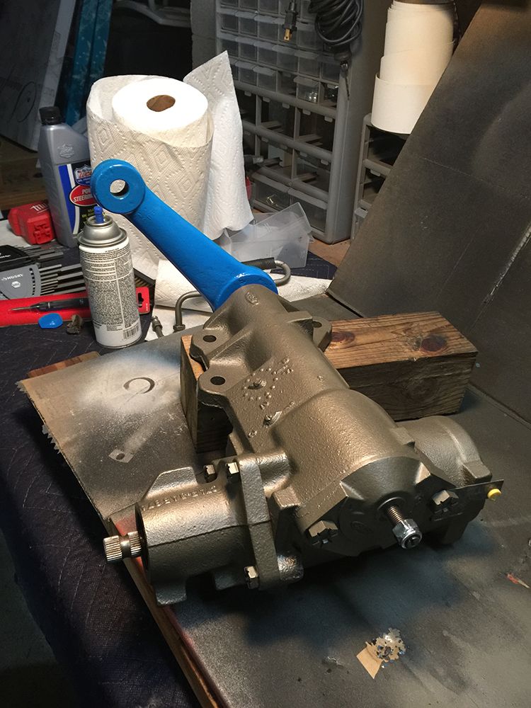 Rebuilt power steering gearbox with blue pitman arm on a workbench.