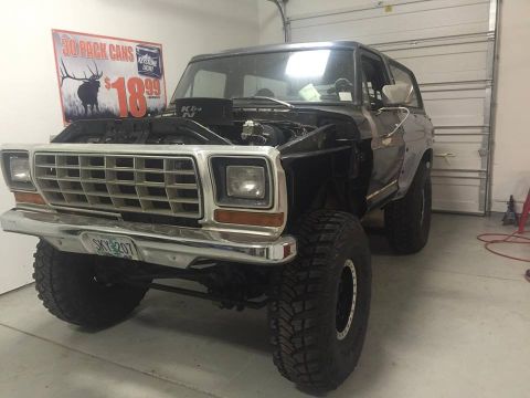 1979 Ford Bronco - A lifted 1979 Ford Bronco with its hood open is parked in a garage. The front of the vehicle shows a chrome grille, large off-road tires, a…