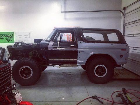 1979 Ford Bronco - Side view of a modified Ford Bronco in a garage. The vehicle has large off-road tires, a lifted suspension, and appears to be undergoing so…