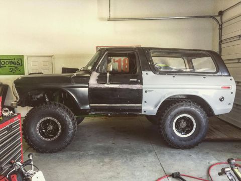 1979 Ford Bronco - A black and silver Ford Bronco is parked in a garage with large off-road tires. The vehicle appears to be undergoing modification or repair…