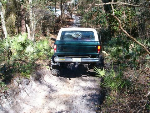 1991 Ford Bronco - A lifted green Ford Bronco navigates a wooded trail, with another white vehicle visible in the distance.