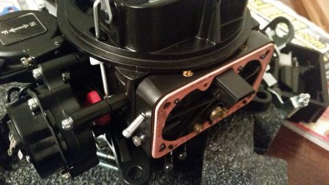 1981 Ford Bronco - A black aftermarket carburetor is shown with a pink gasket installed. The carburetor has various metal and plastic components attached, inc…