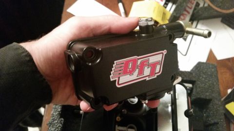 1981 Ford Bronco - A person is holding a black DFT fuel pressure regulator with a silver fitting and a hose barb. The regulator has a red and white DFT logo o…