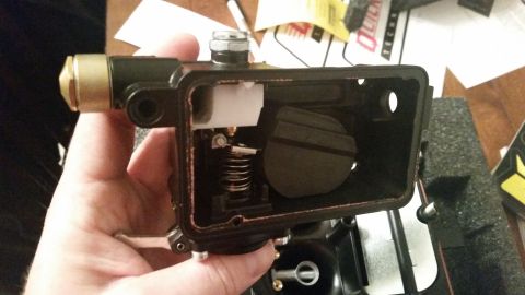 1981 Ford Bronco - A person's hand is holding a disassembled carburetor with a black housing and a brass fitting. Inside the housing, a dark float and a metal…