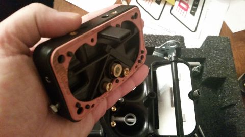 1981 Ford Bronco - A hand holds a disassembled carburetor with a copper gasket. The carburetor is black with brass fittings and is shown partially assembled w…