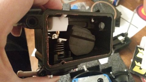 1981 Ford Bronco - A person's hand holds a disassembled carburetor float bowl assembly, revealing the float, spring, and needle valve mechanism.