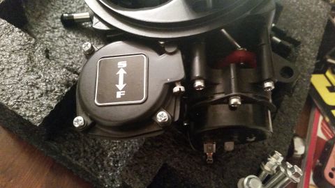 1981 Ford Bronco - A black automotive throttle body is shown, resting on black foam packaging. A silver emblem with white arrows and the letters "S" and "F" i…