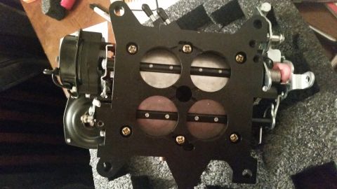 1981 Ford Bronco - A black four-barrel carburetor is shown from a top-down perspective, resting on a textured surface. The carburetor features four circular o…