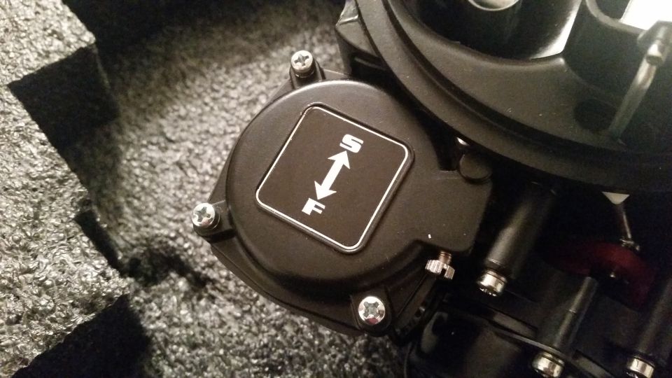Close-up of a black vehicle part with an S/F emblem and arrows.