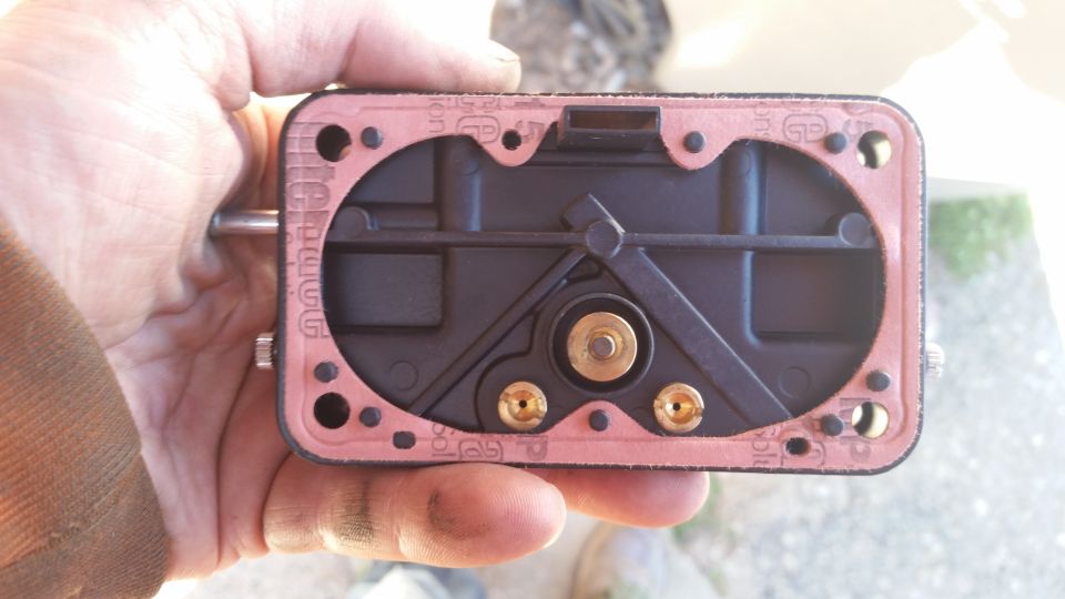 Carburetor base with pink gasket held by a hand.