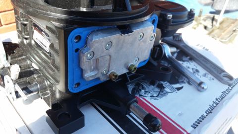1981 Ford Bronco - A close-up view of a black carburetor with a blue gasket and a silver plate with screws. Tools, including a wrench and a ratchet, are visib…