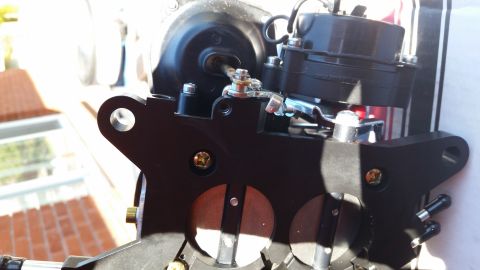 1981 Ford Bronco - A close-up, angled shot shows a black metal automotive part, likely a carburetor or throttle body, with visible screws, linkages, and circu…